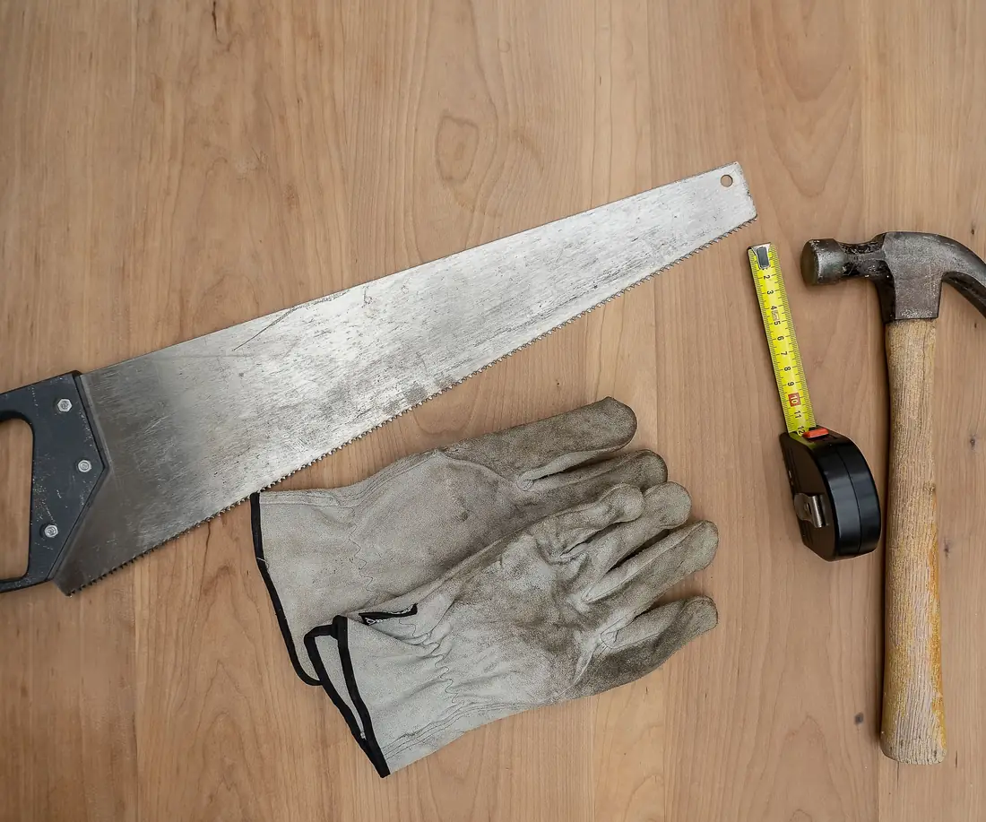 Saw, hammer, tape measure and work gloves on a wooden surface