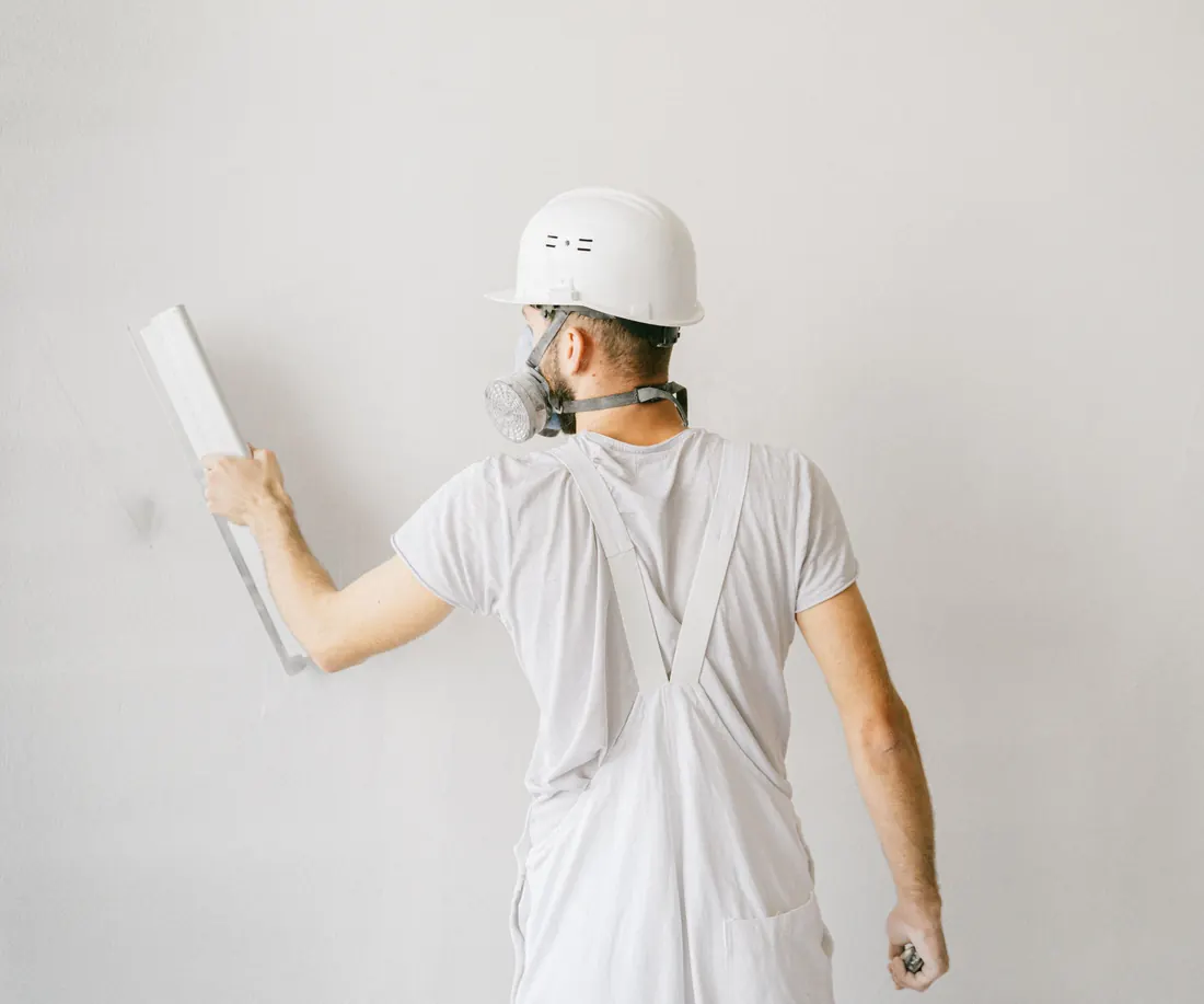 Plasterer in overalls smoothing a wall